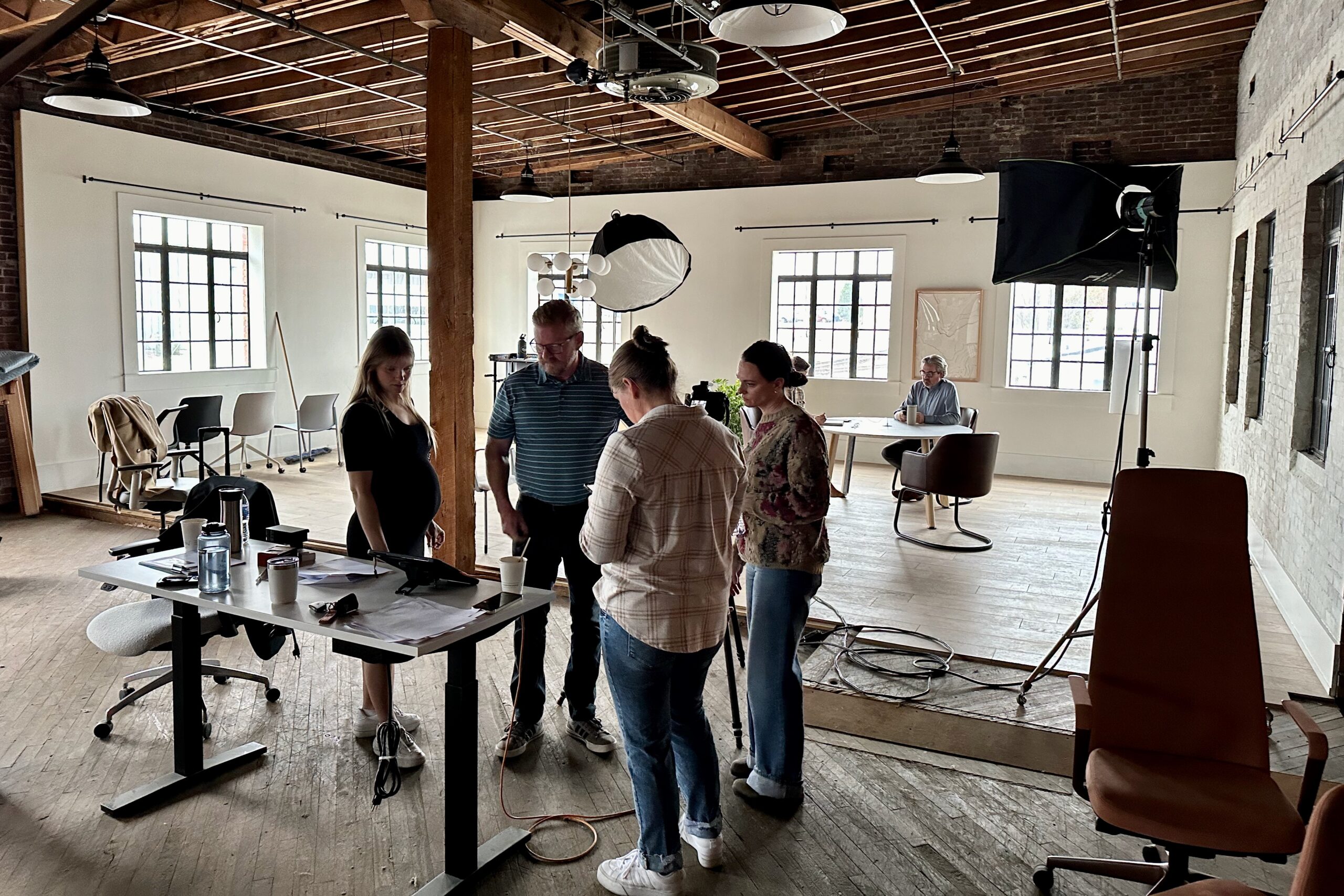 Three women and one man huddle together looking at a digital tablet while Jonathan is in the background on the set for the photoshoot.